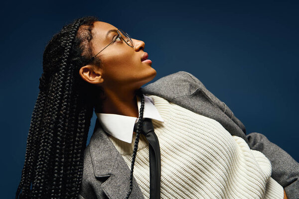 A beautiful young woman showcases her braided hair and stylish outfit while gazing thoughtfully.