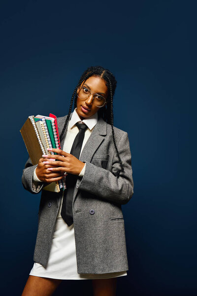 Confident young woman poses with books, flaunting her unique style against a dark backdrop.
