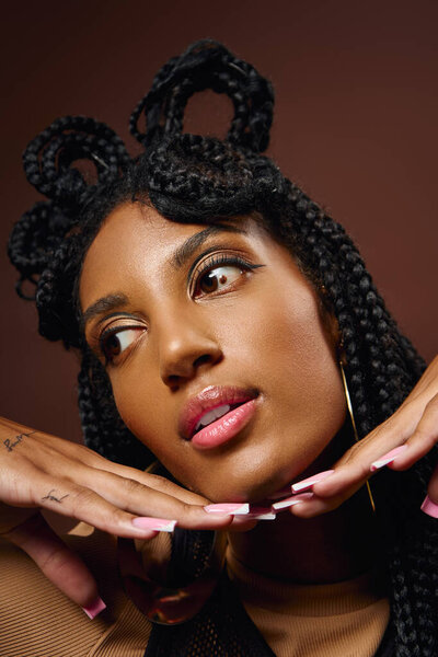 A young woman elegantly shows off her unique braided hairstyle with her hands under her chin.
