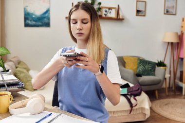 A teenage girl is focused on her smartphone in a stylish room filled with personal touches. clipart