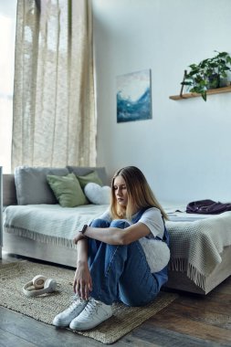 Genç bir kız rahat bir şekilde yerde oturuyor, dekorla dolu şık odasını yansıtıyor..