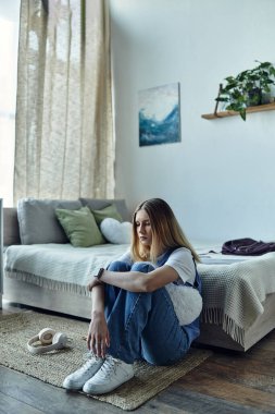 A teenage girl sits comfortably on the floor, reflecting in her stylish room filled with decor. clipart