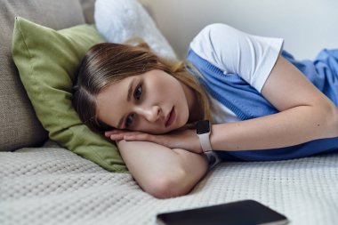 Şık bir dairede, genç bir kız yatağında uzanıyor, telefonu yakınlarda bir yerde, düşüncelere dalmış..