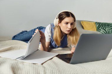 Genç bir kız laptopuna odaklanmış, yanında notlarla kendini çalışmaya veriyor..