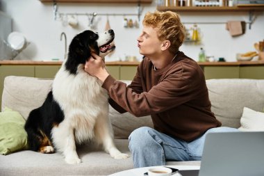 Kızıl saçlı genç bir adam, sıcak bir yerde köpeğiyle sevgi dolu bir anı paylaşıyor..