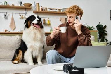 Young man relaxed at home, sipping coffee while talking on his phone with his dog beside him. clipart