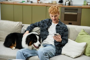 Genç bir adam şık bir dairede neşeli köpeğiyle kanepede uzanıyor..