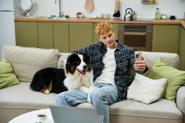 Genç bir kızıl saçlı adam, sevimli Avustralyalı çoban köpeğiyle evde vakit geçirmekten zevk alıyor..
