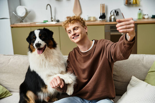 Молодой рыжий мужчина наслаждается уютным моментом со своим австралийским пастухом в их современной квартире.