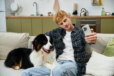 Genç adam, sevimli Avustralyalı çobanıyla şık bir evde neşeli bir selfie çekiyor..