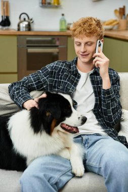 Kızıl saçlı genç bir adam köpeğini okşayan bir telefon görüşmesi yapıyor..