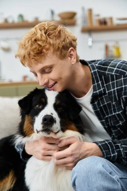 A cheerful young man with red hair shares a tender moment with his Australian Shepherd at home. clipart