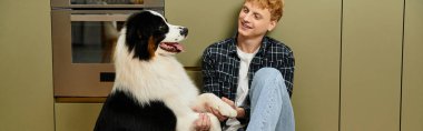 Evde dinlenen genç kızıl saçlı bir adam köpeğiyle neşeli bir anı paylaşıyor, afiş.