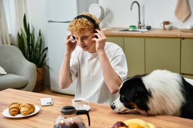Genç kızıl saçlı adam kahvesini yudumlarken ve hamur işlerinin tadını çıkarırken Avustralya çobanıyla rahatlıyor..