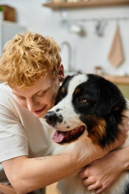 Genç kızıl saçlı bir adam, Avustralyalı çoban köpeğiyle sevgi dolu bir kucaklaşmanın keyfini çıkarıyor..