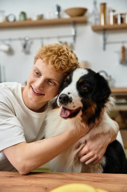 Kızıl saçlı neşeli bir genç, modern uzayda sevimli Avustralyalı çoban köpeğini kucaklıyor..