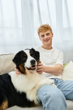 Kızıl saçlı genç bir adam evde rahatlıyor, sevimli köpeğiyle neşeyle oynuyor..