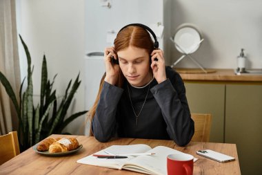 Modern bir dairede dinlenen genç bir adam, masasında çalışırken müzik dinler..