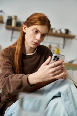 Uzun kızıl saçlı şık genç adam akıllı telefonunu evde kullanırken koltukta dinleniyor..