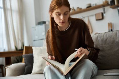 Kızıl saçlı adam evdeki modern yaşam alanında kitap okuyarak sakin vakit geçirmekten hoşlanıyor..