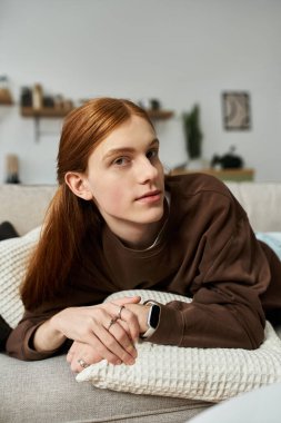 Uzun kızıl saçlı, rahat bir şekilde kanepede uzanan sıradan bir genç. Tarzı rahatlatıcı..