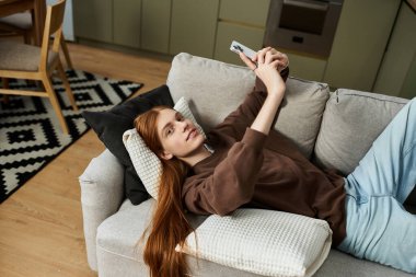 Şık bir genç adam kanepede uzanıyor, rahat bir dairede telefonunu karıştırıyor..