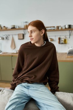 Uzun kızıl saçlı şık bir genç adam şık dairesinde rahat rahat giyiniyor..