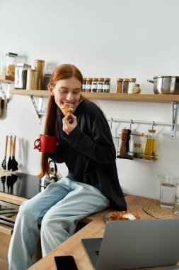 Uzun kızıl saçlı genç bir adam şık dairesinde oturuyor, kahvaltı ve içkinin tadını çıkarıyor..