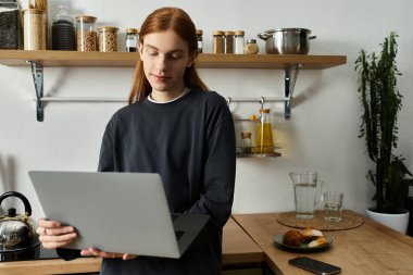 A young man with long red hair relaxes in his trendy apartment while using his laptop. clipart