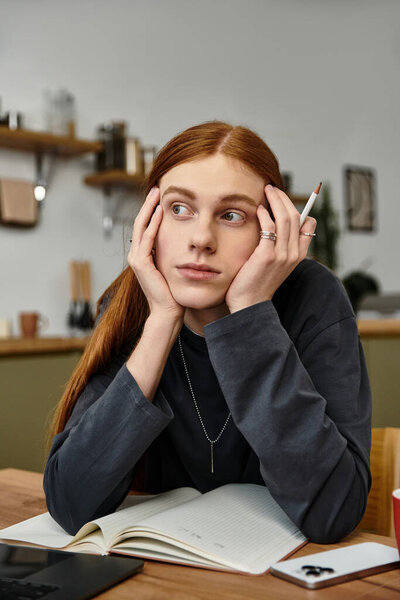 In a modern apartment, a young man with long hair ponders his thoughts while relaxing indoors.