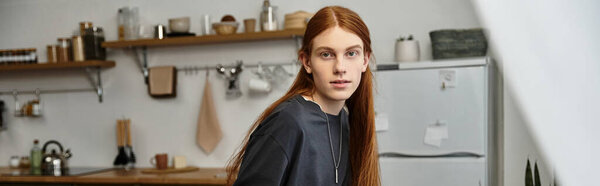 Хороший на вид молодой человек с длинными волосами каскадно отдыхает в своей современной квартире, баннер