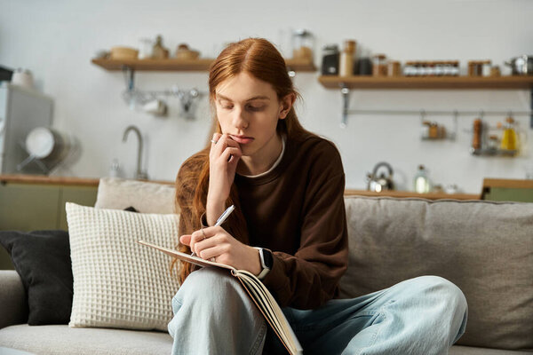 In a stylish apartment, a handsome redhead young man thoughtfully writes notes in his notebook.