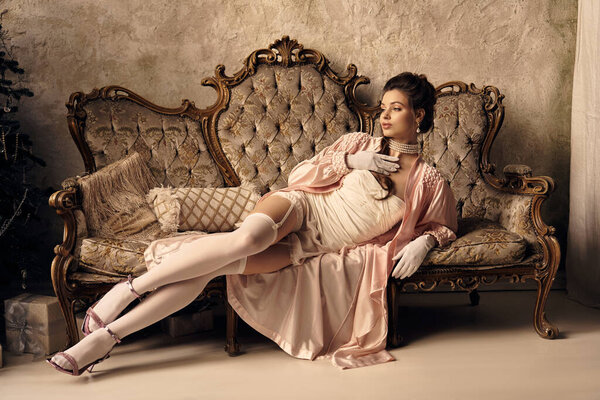 A young woman, like a nymph, relaxes gracefully on an ornate vintage sofa.