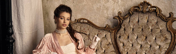 A lovely young woman in a nymph outfit rests gracefully on vintage furniture, radiating charm.