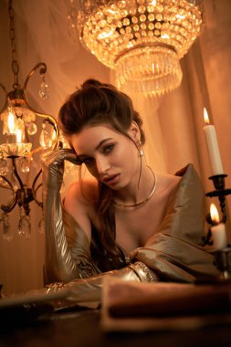 Vampir cazibesine sahip genç ve güzel bir kadın ışıldayan bir avizenin altında zarifçe poz verir..