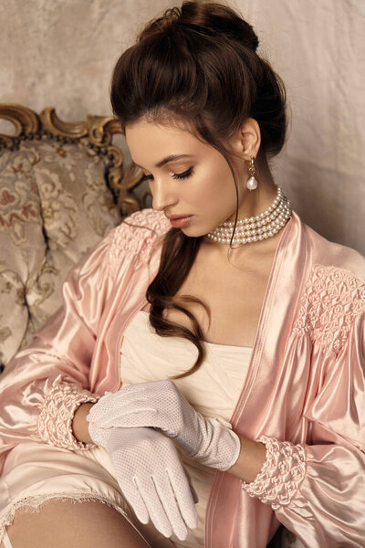 A young woman in a satin robe delicately adjusts her gloves, embodying an ethereal presence.