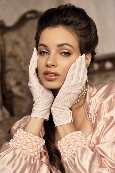 A lovely young woman poses gracefully in a dreamy vintage setting, wearing elegant gloves.