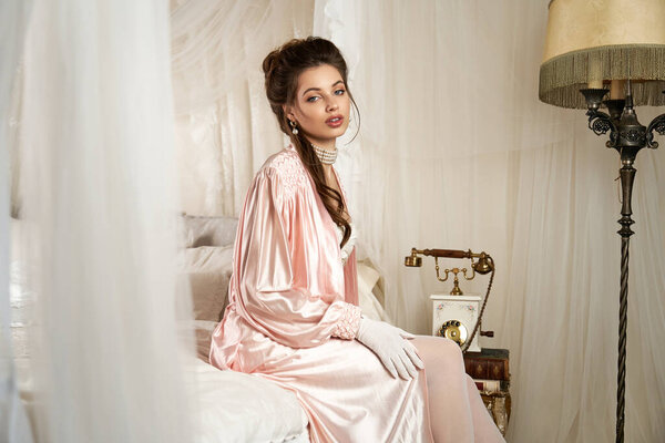 A young woman in vintage clothes sits gracefully on a bed, radiating a mystical aura.