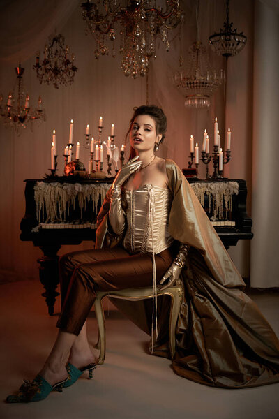 A young woman embodies a mystical vampire in an elegant ballroom, surrounded by flickering candles.