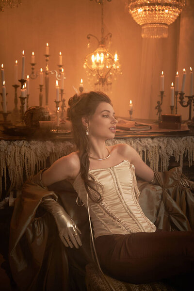 A striking young woman captivates in a candle lit room with her graceful attire.
