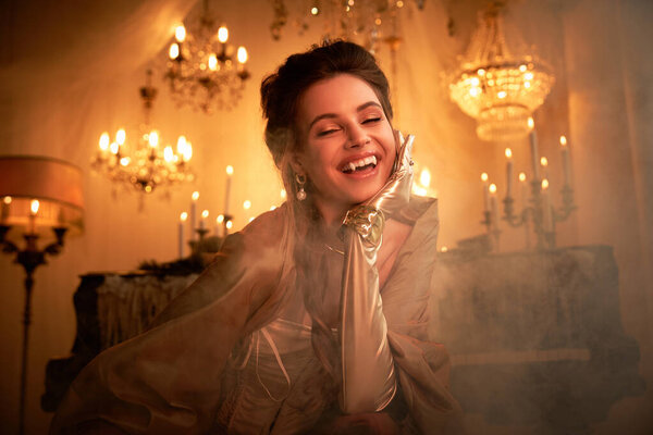 Красивая девушка радостно улыбается, окруженная светящимися люстрами и туманной атмосферой.