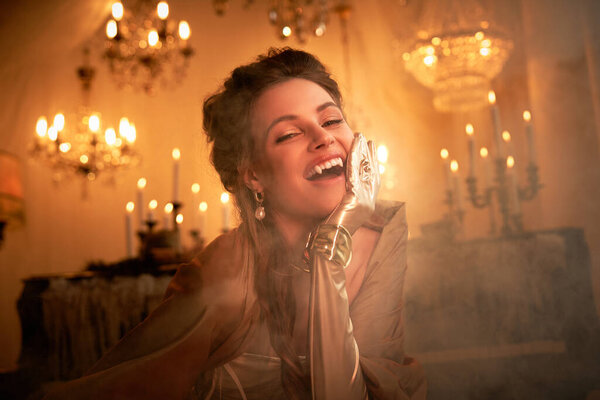 In a dim, elegant room with chandeliers, a young woman embodies a charming vampire.
