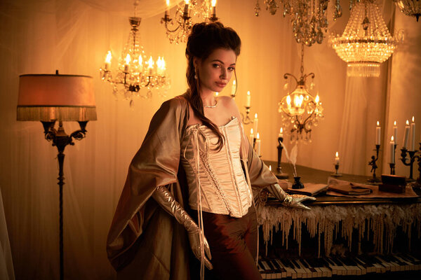 Молодая женщина обнимает свою вампирскую личность в щедро освещенной комнате с люстрами.