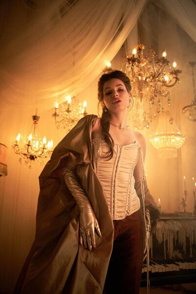 Молодая женщина источает мистическую ауру вампира в тускло освещенной, роскошной комнате с люстрами.
