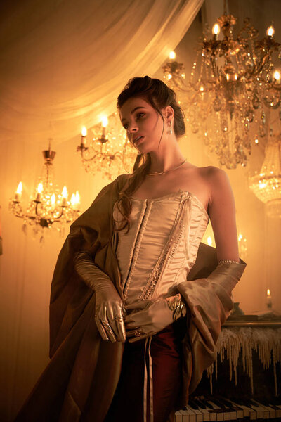 A beautiful young woman embodies a vampire in a lavish ballroom bathed in warm light.