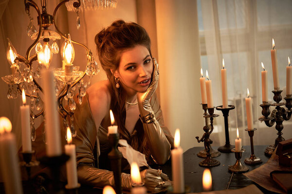 A young woman embodies a mystical vampire, illuminated by candles, exuding elegance and intrigue.