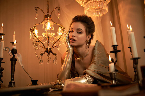 A captivating young woman with elegant features exuding a vampire allure, surrounded by candlelight.