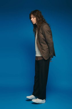 Şık giyinmiş genç adam kendine güvenerek duruyor, modern moda estetiğini somutlaştırıyor.