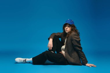 Şık giyinmiş genç bir adam mavi arka planda rahatça uzanır..