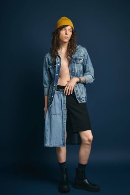 Şık bir genç adam sağlam bir arka plana karşı duruyor, eşsiz kot pantolon moda tercihleri sergiliyor..